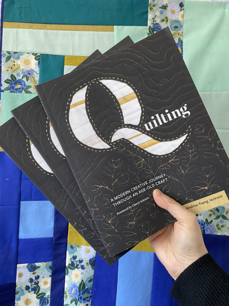 A hand holds a book titled Quilting by Andrea Tsang Jackson