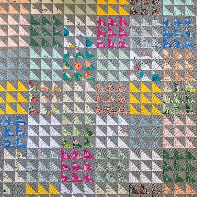 close up view of a quilt made of half square triangles in shades of gray pink yellow and blue