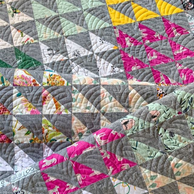 close up view of a quilt folded on itself made of half square triangles in shades of gray pink yellow and blue