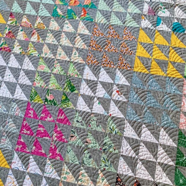 close up view of a quilt made of half square triangles in shades of gray pink yellow and blue