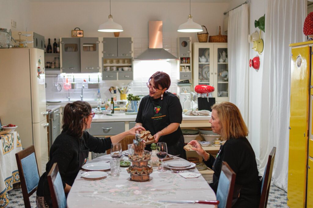 A woman shares a plate of bread with two women at. table in her kitchen