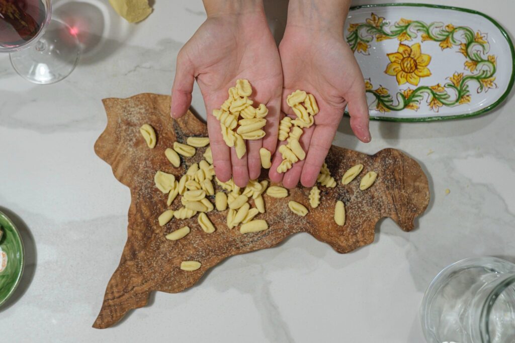 Hands hold homemade cavatelli pasta over a cutting board in the shape of Sicily