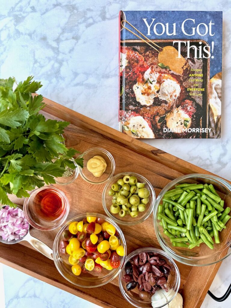 You Got This! Cookbook next to a tray of ingredients including green olives, strignbeans, tomatoes, vinegar, parsley and onion