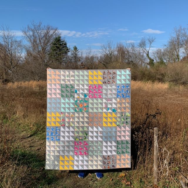 A quilt made of half square triangles hanging in a field
