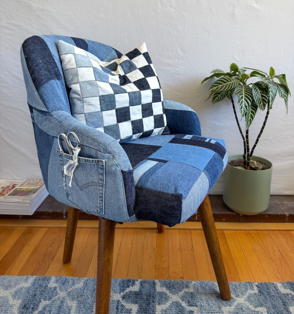 A chair upholstered with various shades of denim with a checkered denim pillow on top.