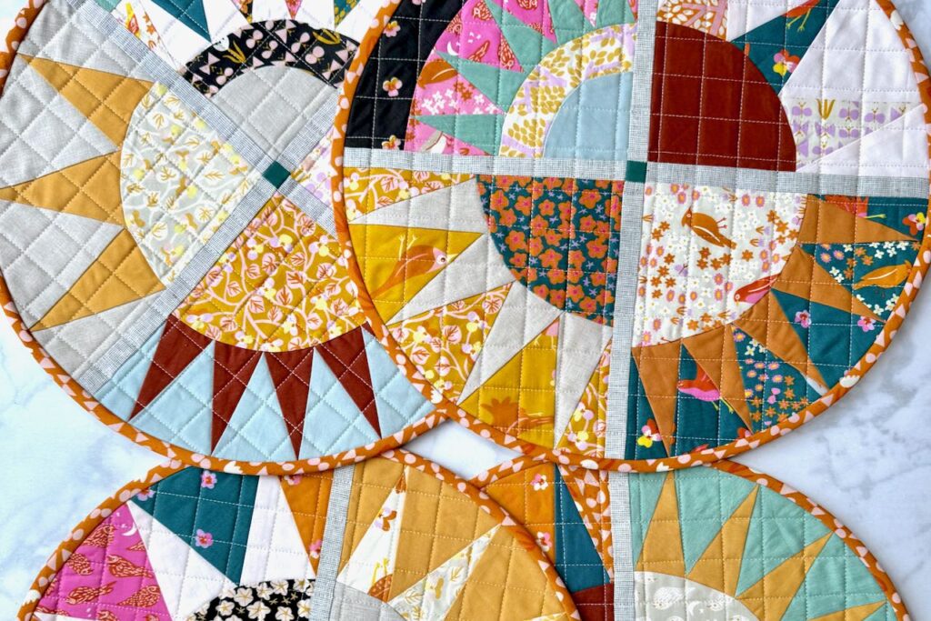 Close-up view of quilted sunburst NY beauty placemats showing detailed fabric patterns by Ruby Star Society and quilting stitches in a grid.