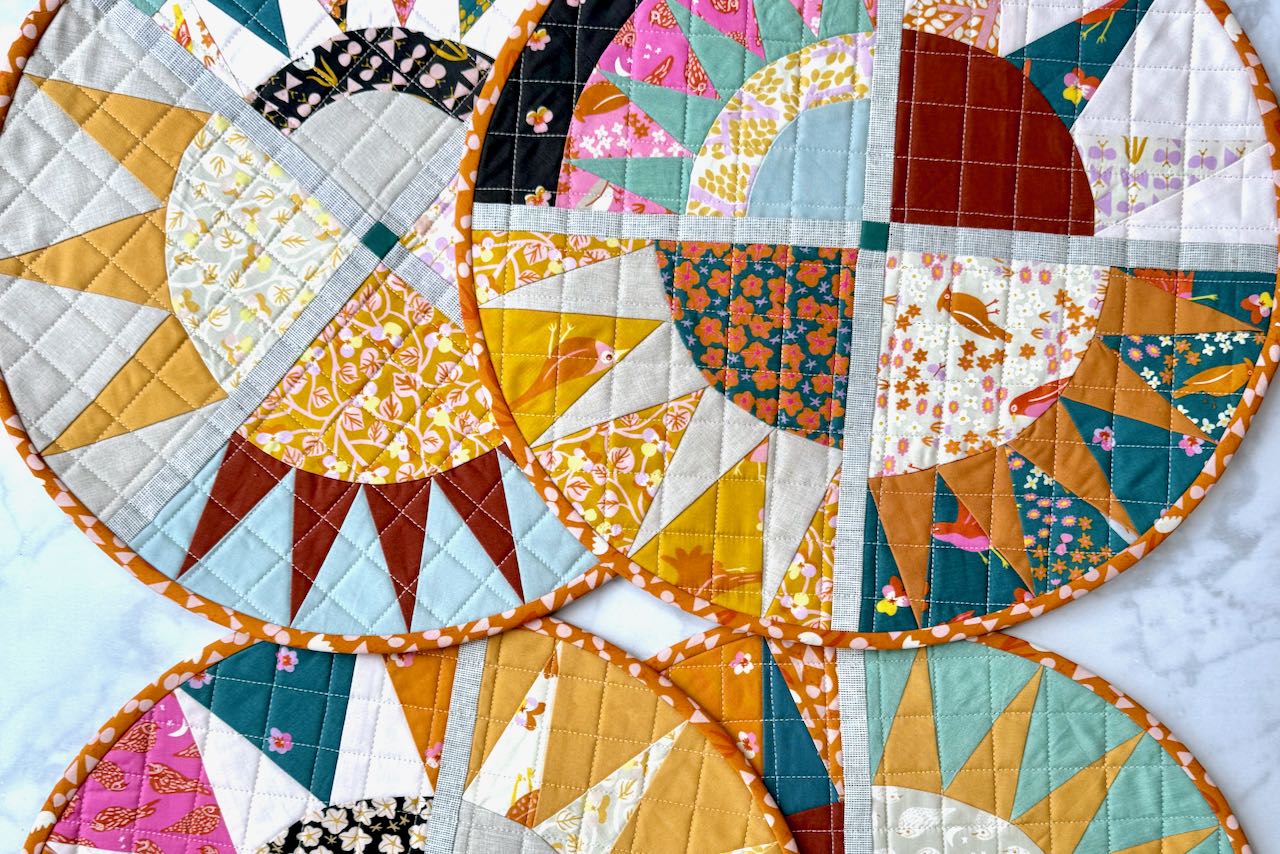 Close-up view of quilted sunburst NY beauty placemats showing detailed fabric patterns by Ruby Star Society and quilting stitches in a grid.
