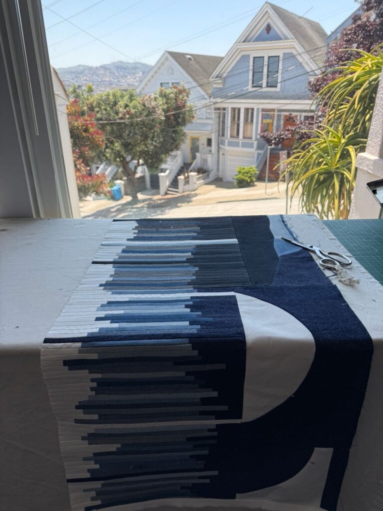 A quilt made with varying shades of denim sits on a table in front of a window overlooking a San Francisco street