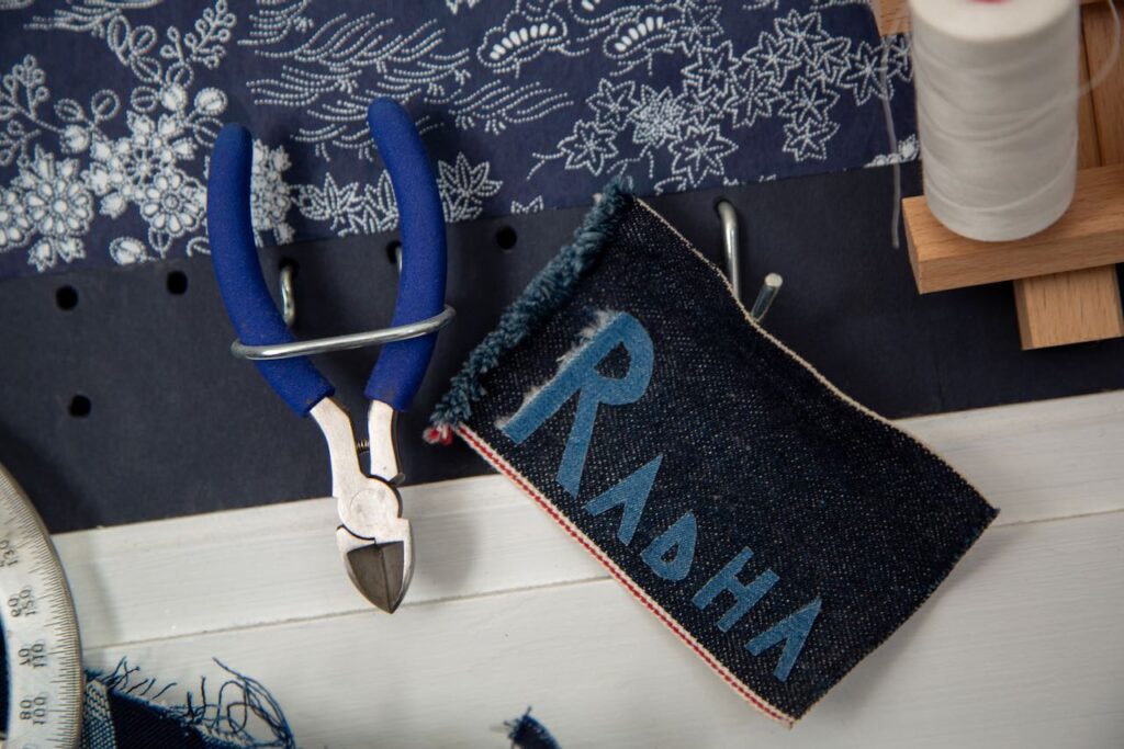 A handmade name tag that says "Radha" next to a pair of pliers leaning on the shelf of a sewing machine.