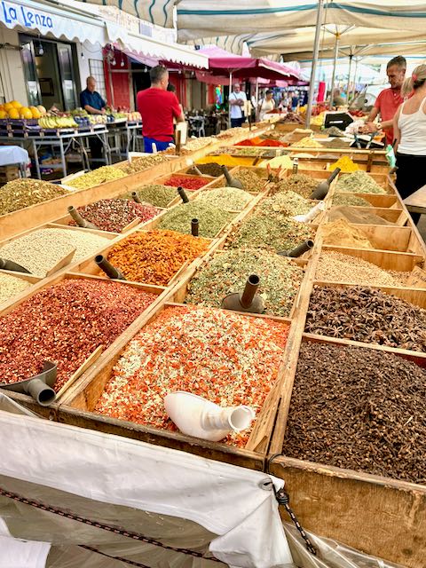 Spices in an assortment of colors look like blocks of orange green and brown in an outdoor market in Siracusa Sicily.